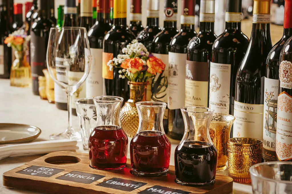 Wooden wine flight with three labeled red wine carafes and bottles.