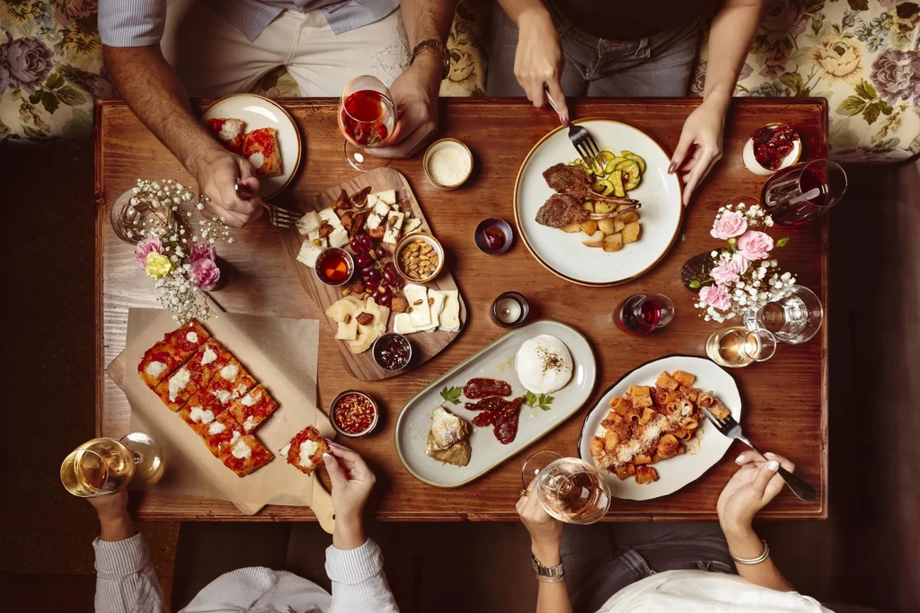 Overhead shot of a dining table laden with diverse shared food and wine.