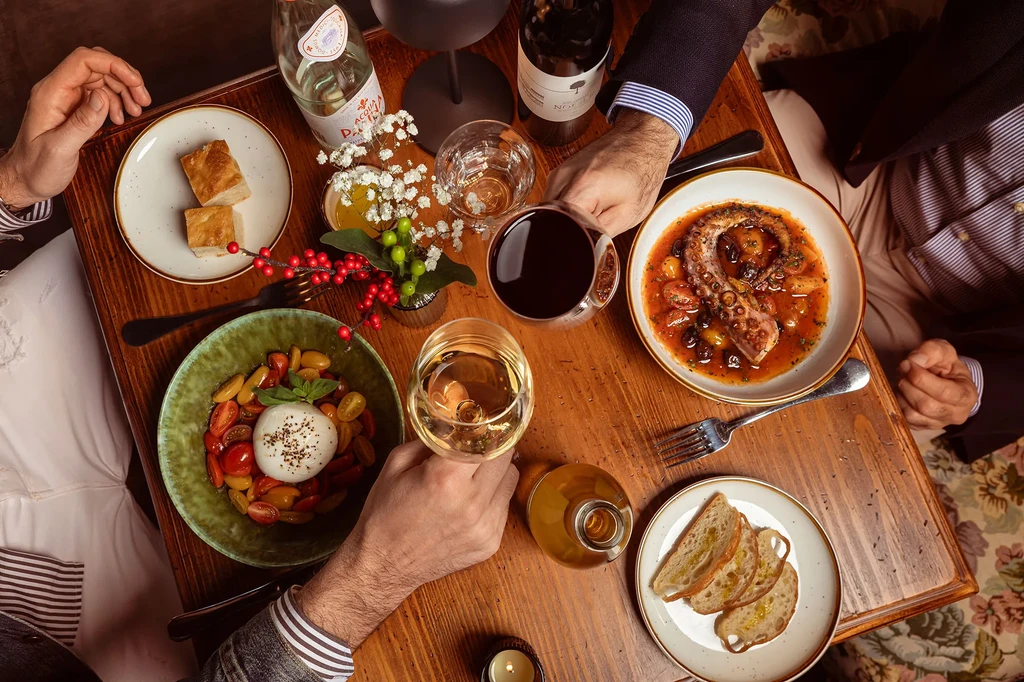 Italian dinner with octopus, burrata, focaccia, and wine, viewed from above.