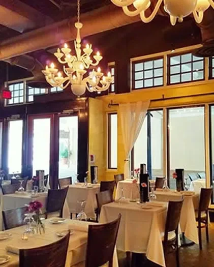 Empty restaurant dining room with set tables, chandelier, and yellow walls.