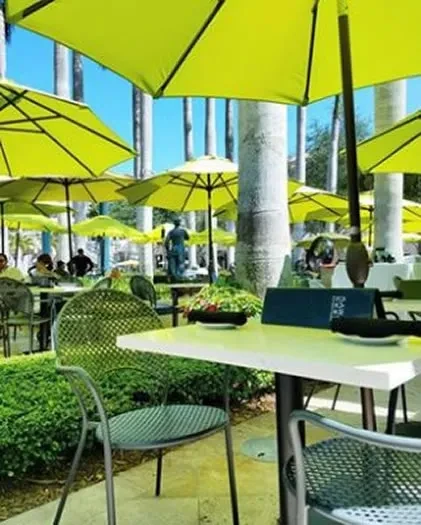 Lime-green umbrellas shade a bright outdoor cafe patio with palm trees.