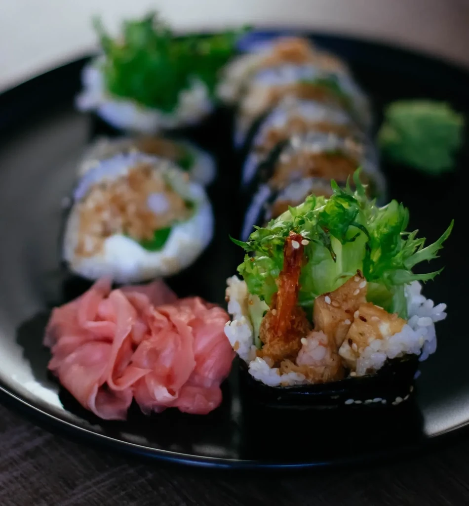 Close-up of a sushi plate with tempura roll, lettuce, ginger, and wasabi.