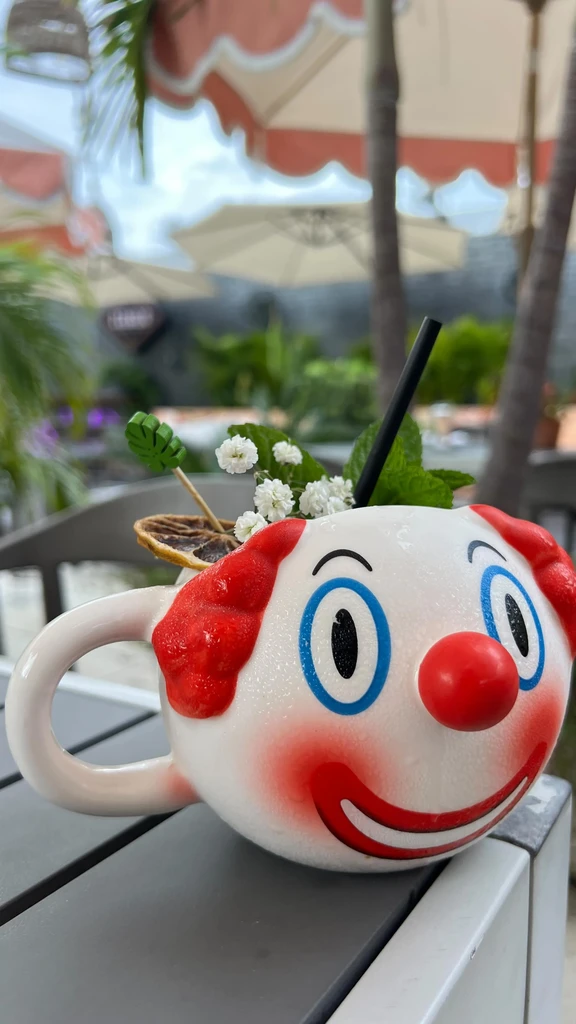 Novelty drink in a clown-head mug with garnishes, outdoors.