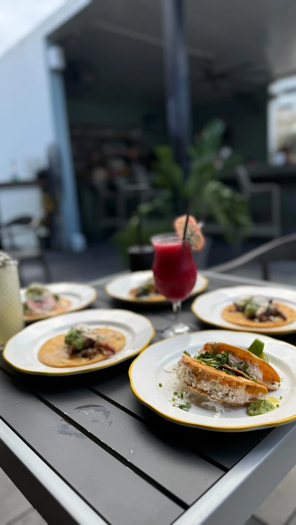 Close-up of several taco plates and drinks on a dark outdoor table.