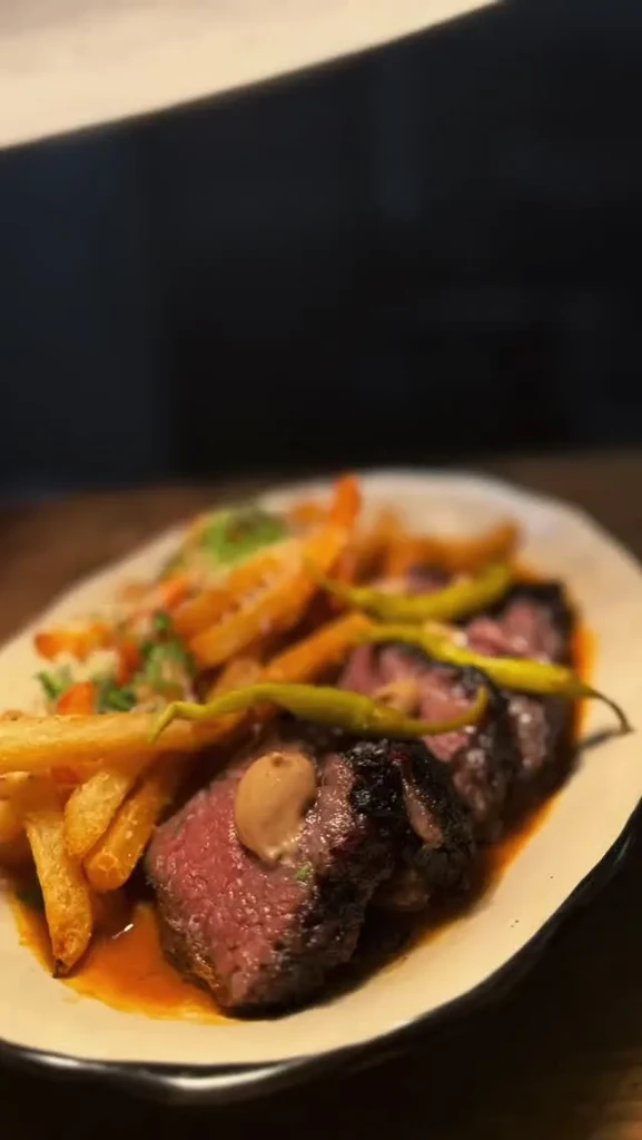 Sliced medium-rare steak, french fries, and green chili peppers on a plate.