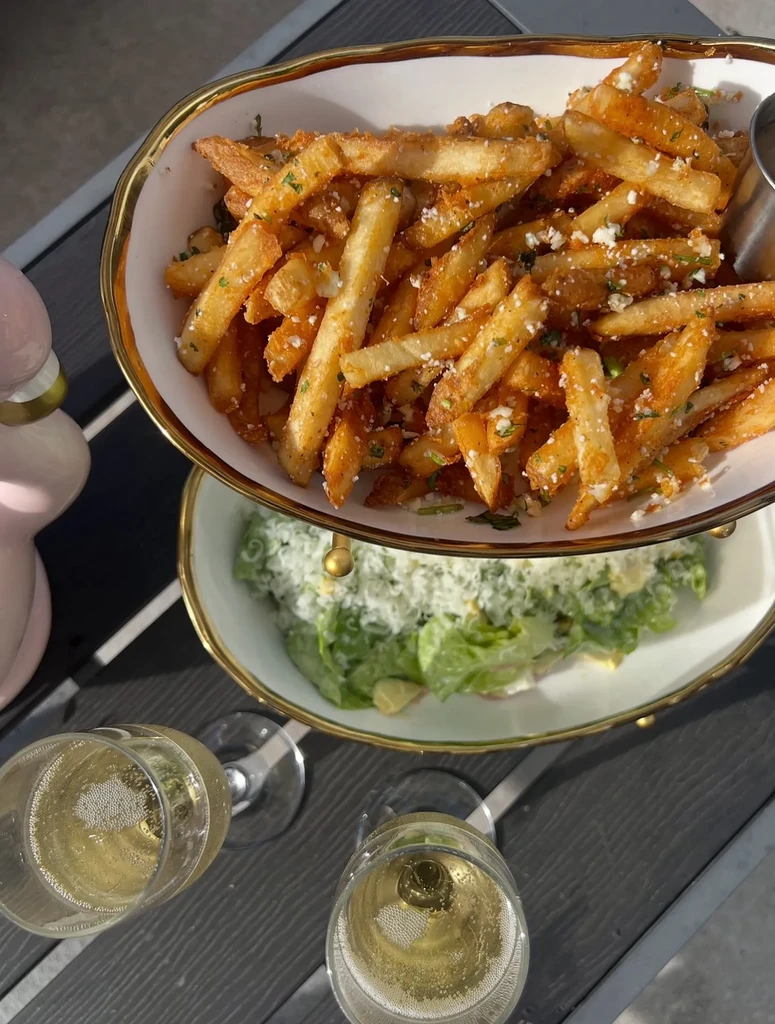 Two-tiered dish with French fries, Caesar salad, and champagne outdoors.