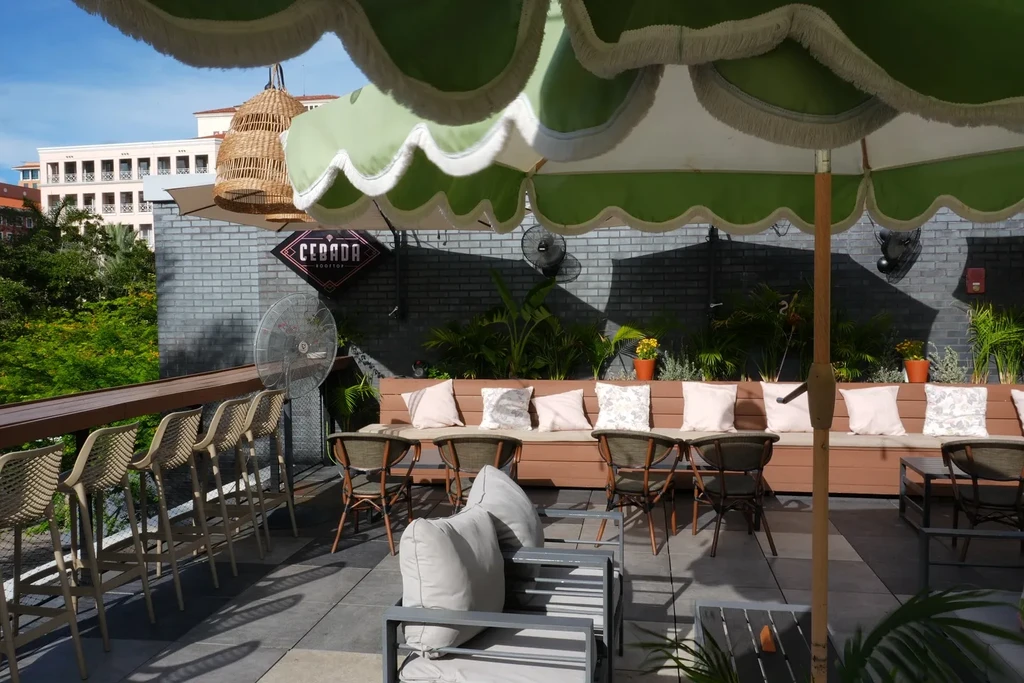 Outdoor rooftop bar patio with green umbrellas and 'CEBADA ROOFTOP' sign.