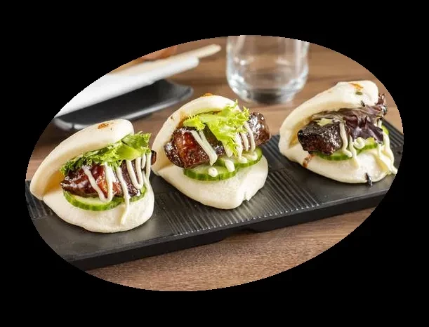 Three pork belly bao buns with lettuce, cucumber, sauce on platter.