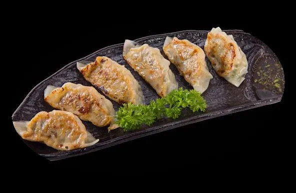 Six crispy gyoza with dipping sauce and green garnish.