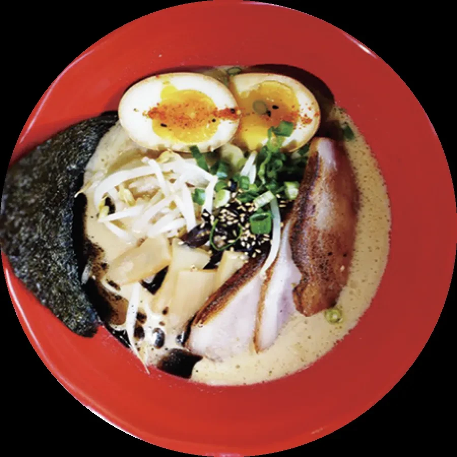 Close-up of vibrant ramen in red bowl with egg, chashu, nori.