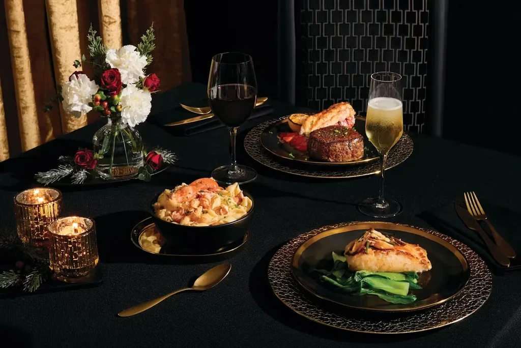 Lavish dining table: steak, lobster, shrimp pasta, fish, wine, and floral decor.