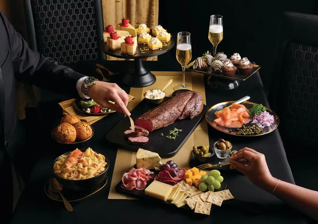 Upscale dining table with roasted meat, charcuterie, desserts, and champagne.
