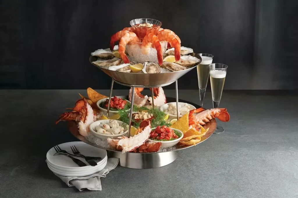 Multi-tiered seafood tower with shrimp, oysters, lobster, and champagne.