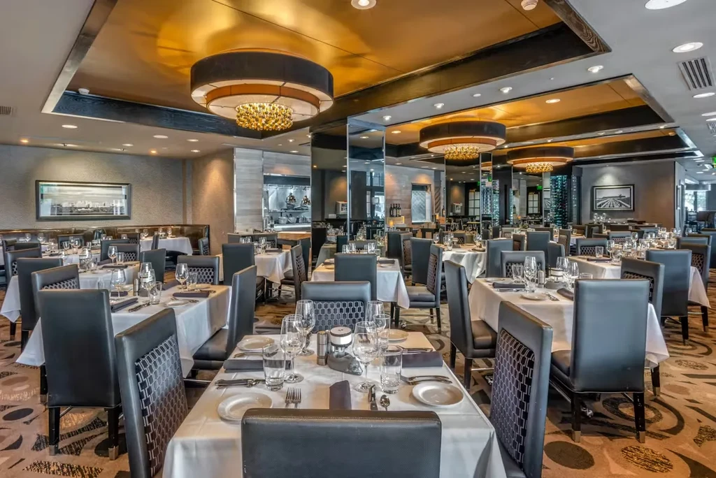 Empty, upscale restaurant dining room with elegantly set tables and chandeliers.