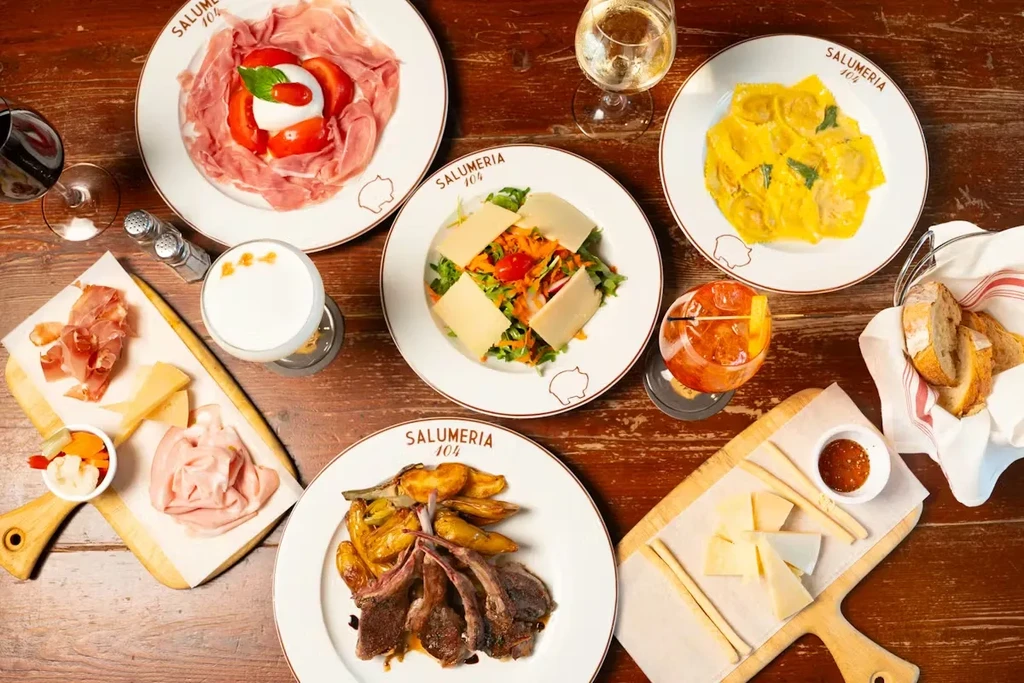 Flat-lay of SALUMERIA 104's Italian charcuterie, pasta, lamb, and drinks.