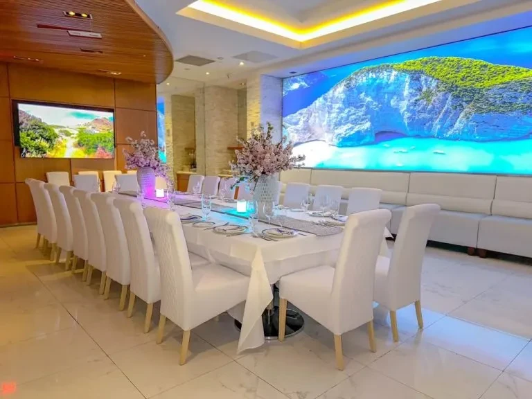 Dining room with set table and large screen displaying scenic bay.