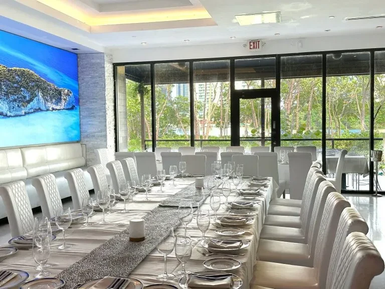 Formal restaurant dining area with set table, large windows, tropical screen.