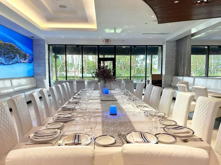 Modern restaurant dining room, formal table, blue lights, sea view screen.