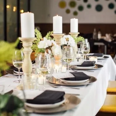 Set dining table with lit candles, white flowers, and formal place settings.