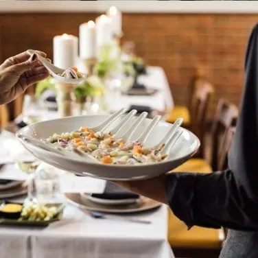 Server presents individual grain appetizers; a hand reaches for one.