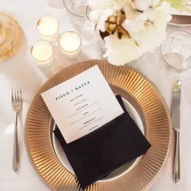 Meticulously set dining table with gold charger, menu, and silverware.