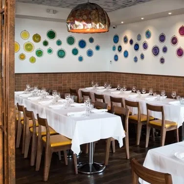 Restaurant dining room with set tables, yellow chairs, colorful wall plates.