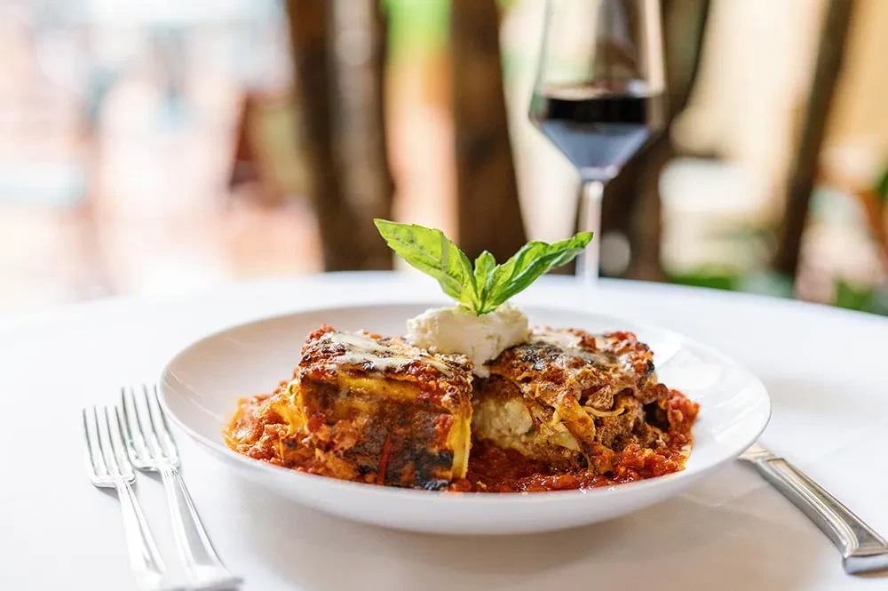 Lasagna in white bowl, topped with melted cheese and basil.