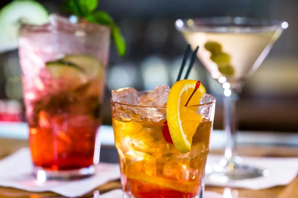 A vibrant orange cocktail with two others on a blurred bar.