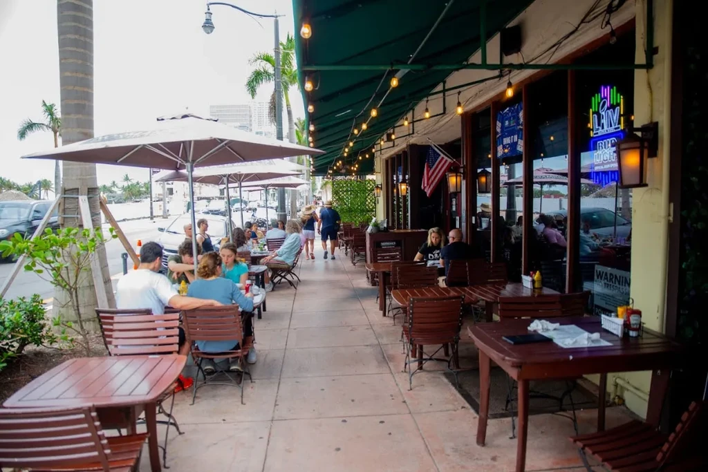 Lively outdoor restaurant patio with green awning and many diners.