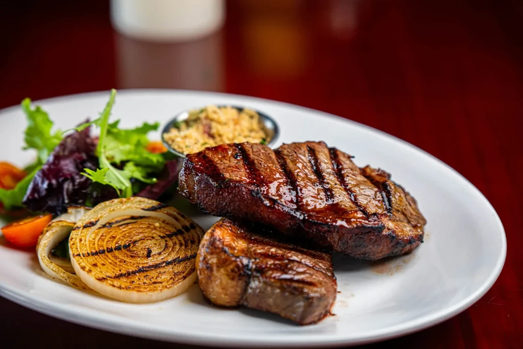 Professionally plated grilled steak, mixed greens, onions, and farofa.