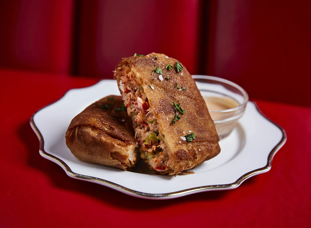 Crispy deep-fried roll halves, seafood-vegetable filling, sauce, red background.