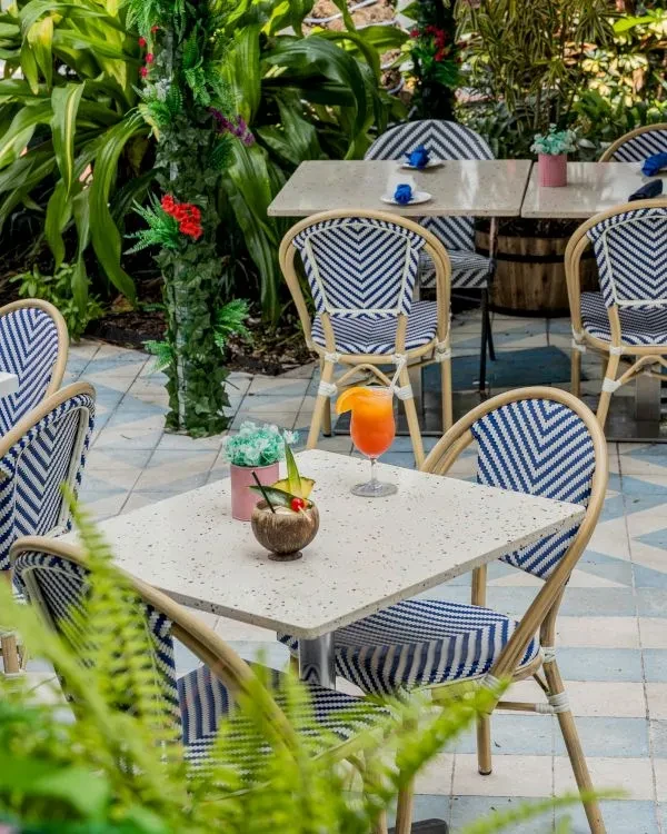 Outdoor patio with patterned chairs, tropical drinks, flowering plants, and tiled floor.