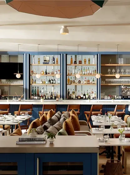 Modern restaurant interior with stocked bar, dining tables, and bench seating.