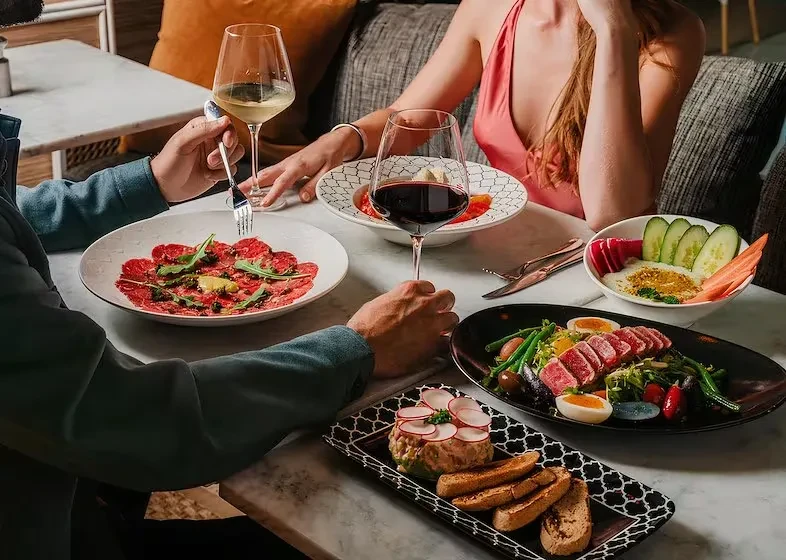 Marble table close-up: two people dining with various dishes and wine.