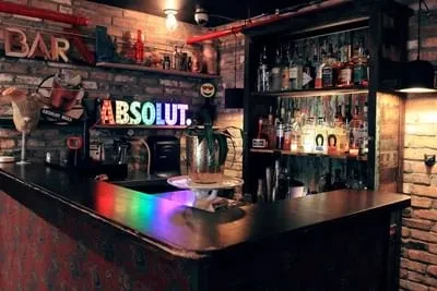 Well-stocked, dark bar with brick wall, industrial pipes, and neon signs.