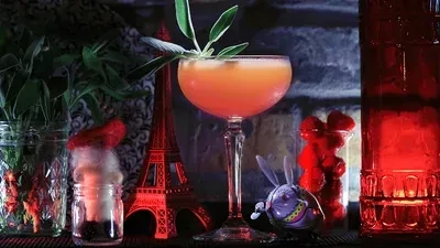 Orange cocktail with herb garnish among glowing, whimsical decorations.