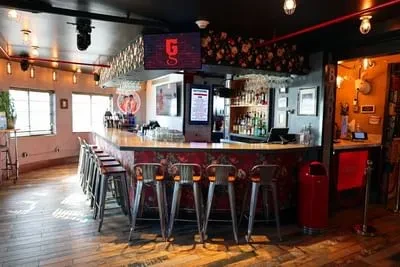 A modern bar with a red floral counter, silver stools, and stocked liquor.