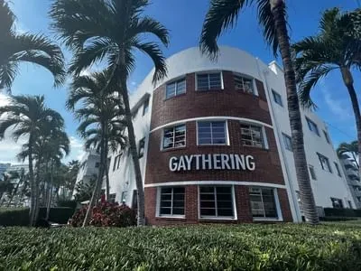 Curved Art Deco building, "GAYTHERING" sign, white and brick, palm trees.