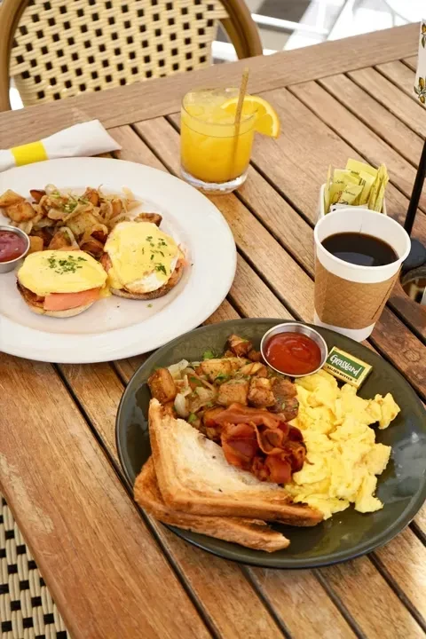 Two breakfast meals on an outdoor table: Eggs Benedict and scrambled eggs.