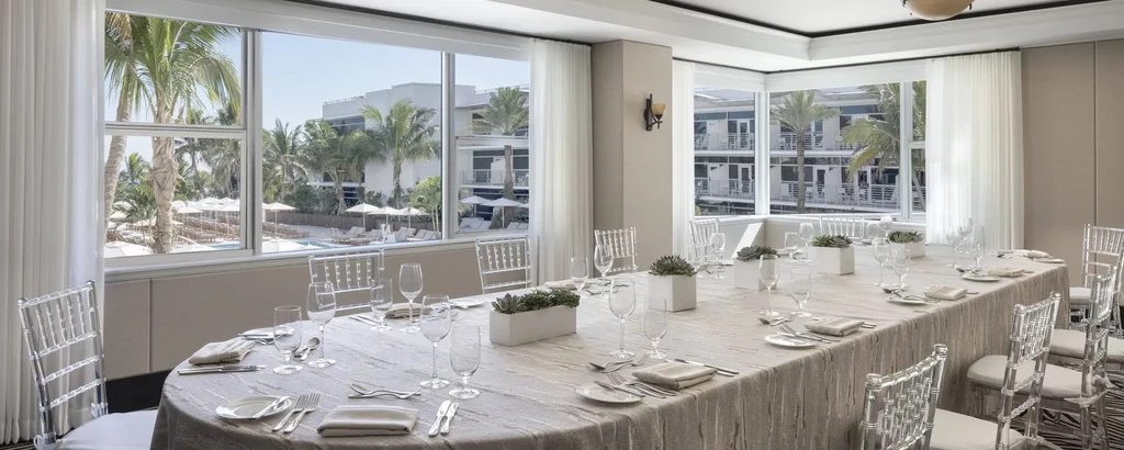 Chic dining room with set table, ghost chairs, and tropical resort view.