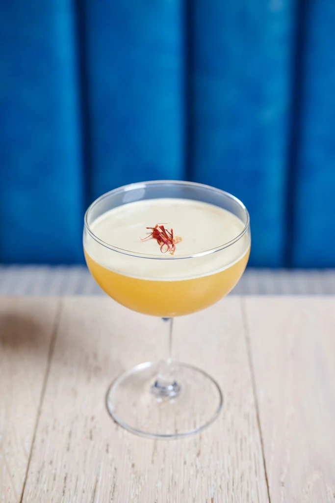 Two-layered cocktail with saffron garnish in a coupe, blue background.