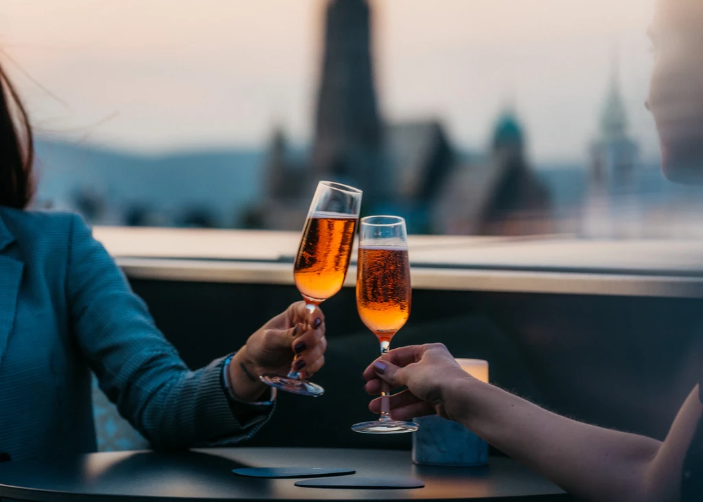Two people clinking champagne flutes against a blurred city skyline.
