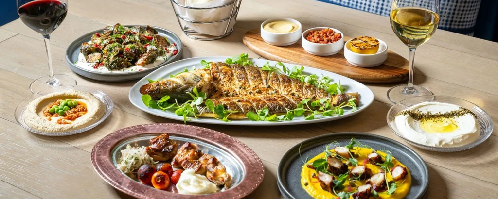 Grilled fish, octopus, roasted vegetables, dips, and wine on a table.