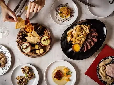 Overhead shot of a table with gourmet dishes and hands dipping chips.