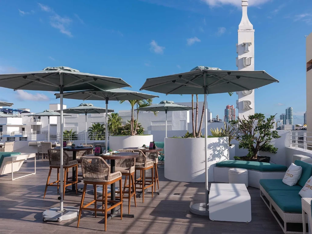 Modern rooftop bar patio with umbrellas, seating, and distant urban skyline.