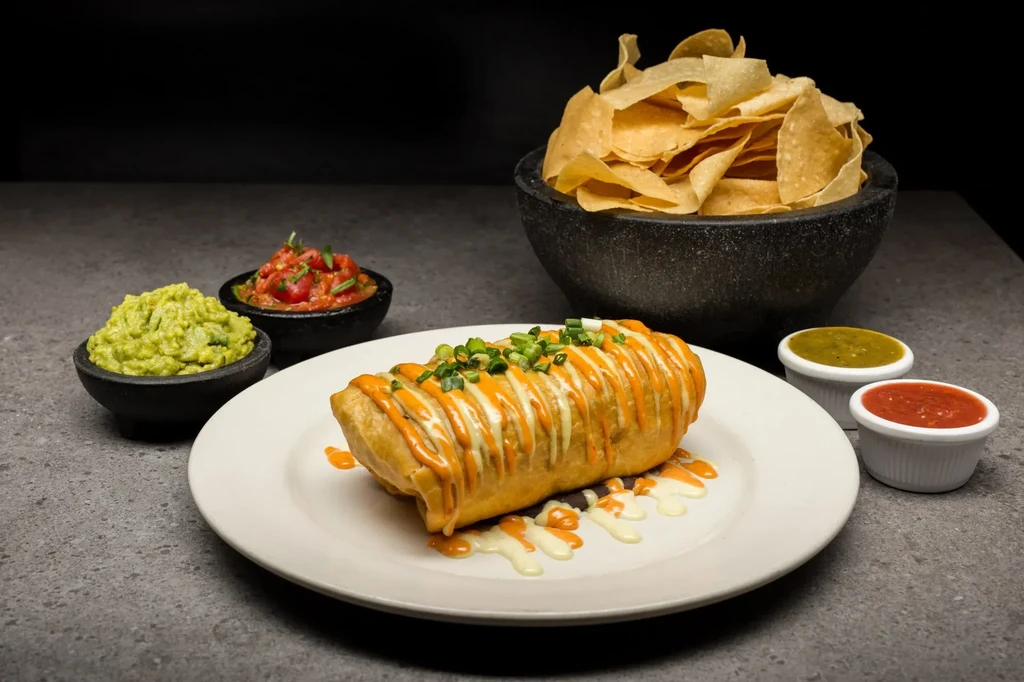 Deep-fried burrito with sauces, guacamole, salsa, and tortilla chips.