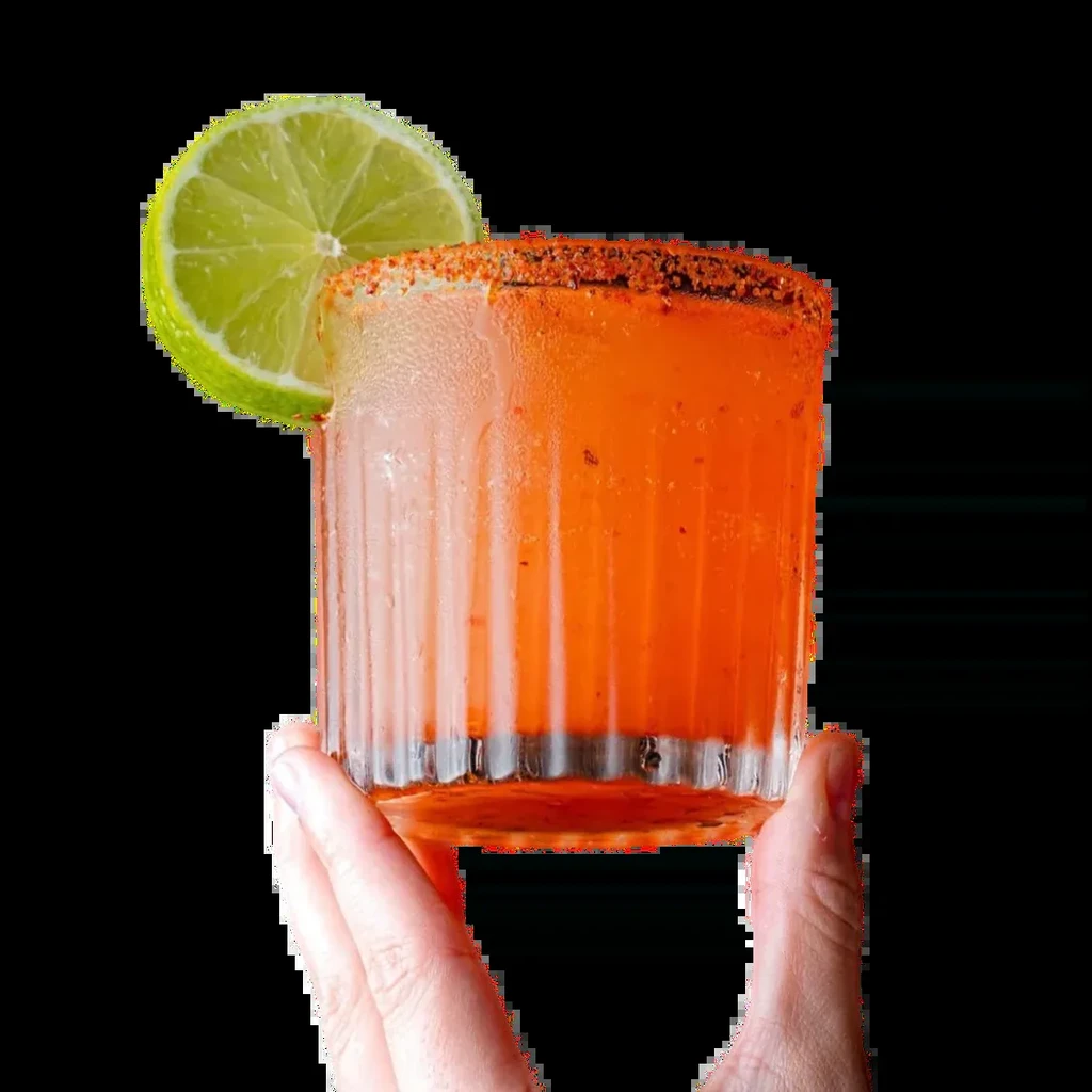 Orange drink in textured glass, chili-lime rim, lime garnish, held.