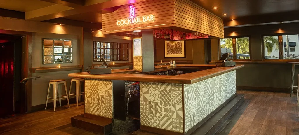Empty cocktail bar with intricate tiled counter and 'COCKTAIL BAR' neon sign.