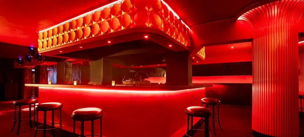 Modern bar interior with a glowing red counter and elaborate ceiling.
