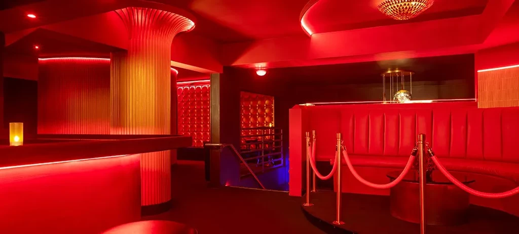 Red-lit upscale lounge interior with plush seating and golden chandelier.